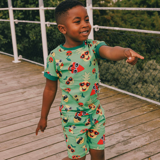 Child wearing a green outfit with fruit patterns on a wooden deck