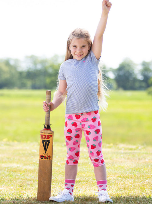 Young girl in strawberry-patterned leggings holding a cricket bat outdoors