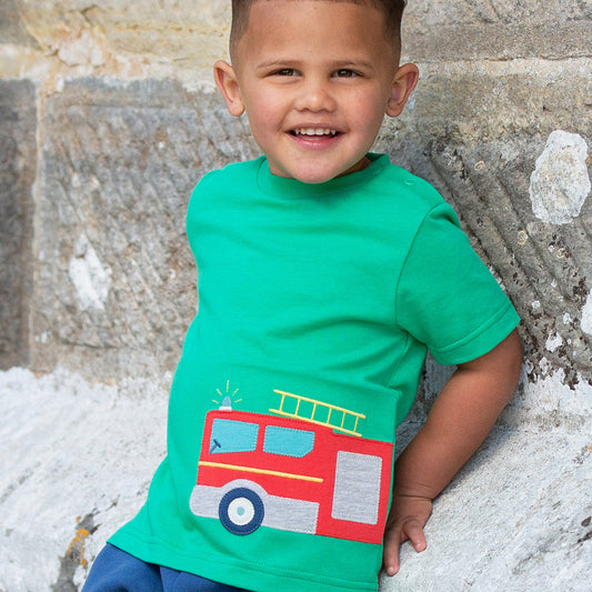 Child wearing a green t-shirt with a red fire truck design against a stone wall.