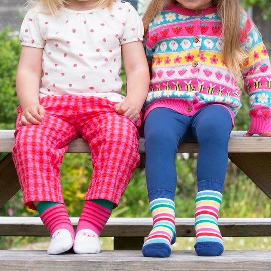 Two young girls sitting on a bench wearing colorful clothing and socks.
