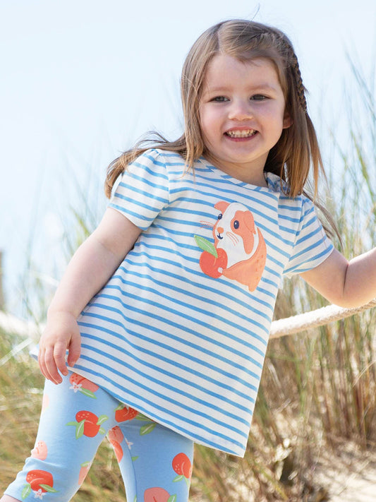 Child wearing a blue and white striped shirt with a guinea pig design, standing in grass.