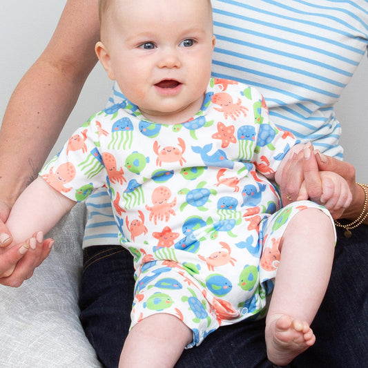 Baby wearing a colorful outfit with sea creature pattern, sitting on a person's lap.