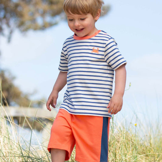 Child wearing a striped shirt and orange shorts standing outdoors.