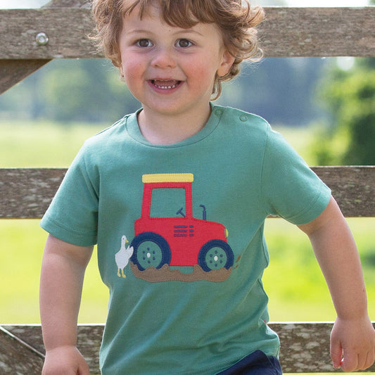Child wearing a green t-shirt with a red tractor design outdoors.