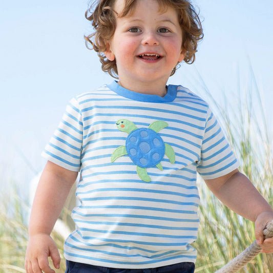 Child wearing a blue and white striped shirt with a turtle design, standing outdoors.