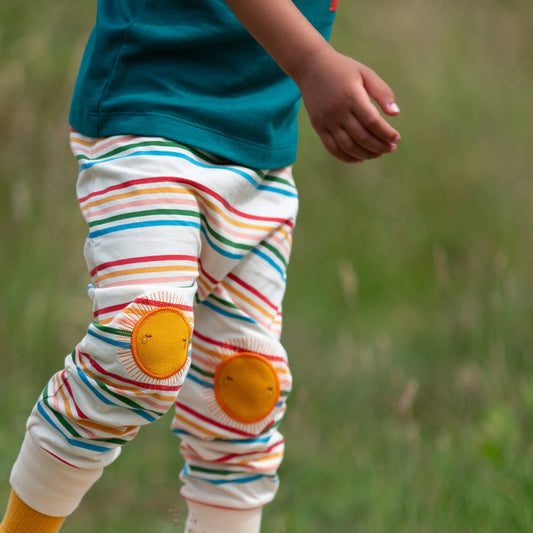 Child wearing colorful striped pants with yellow sun patches in a grassy field