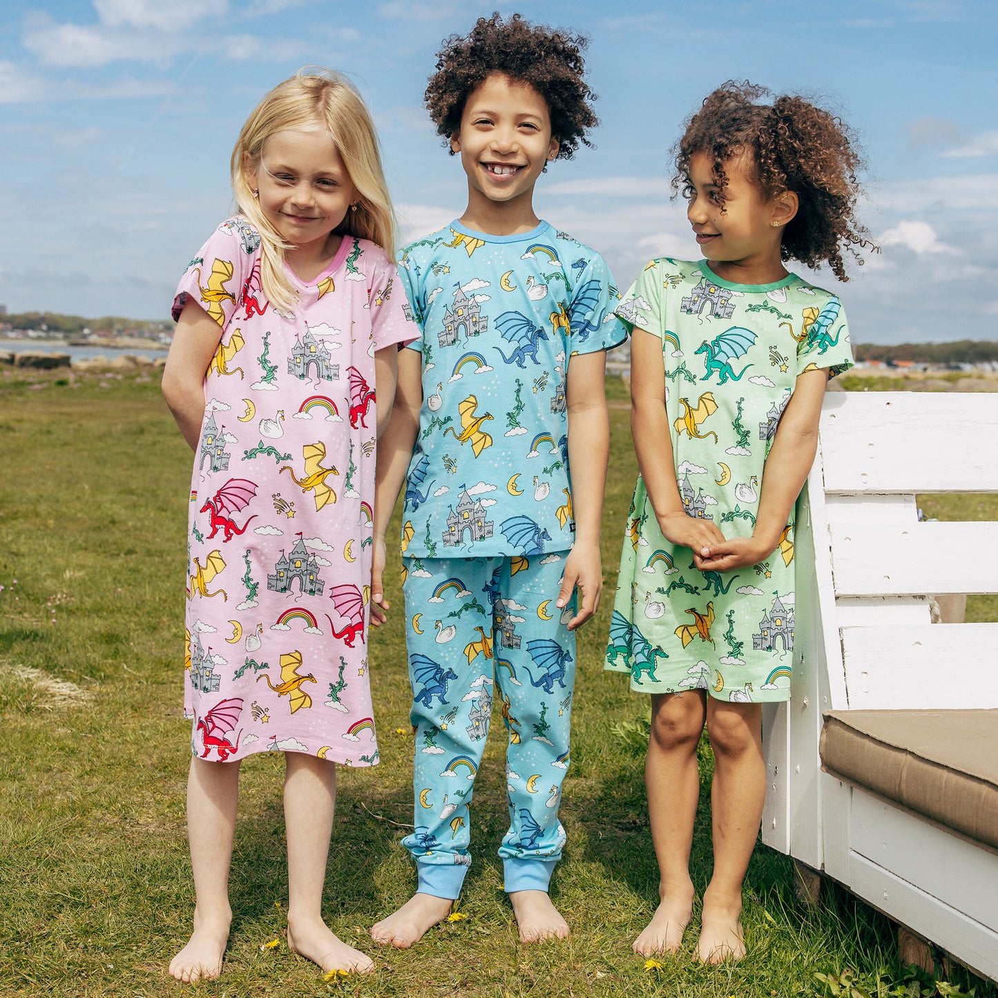 Three children wearing colorful Villervalla pajamas standing outdoors with a bench and grassy area in the background.