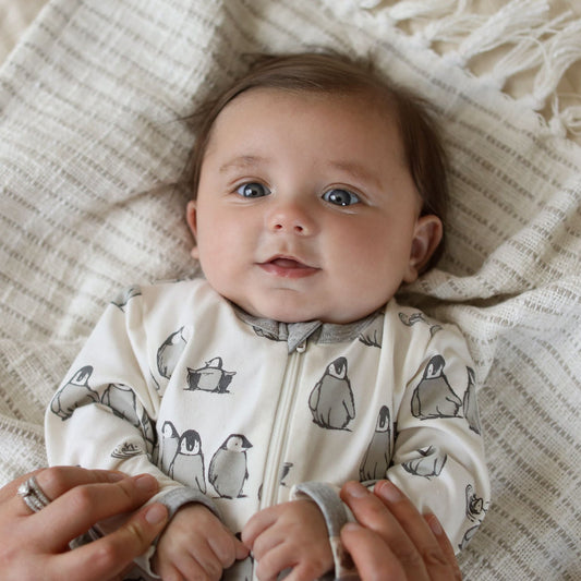 Baby wearing a white onesie with penguin pattern, lying on a textured blanket.