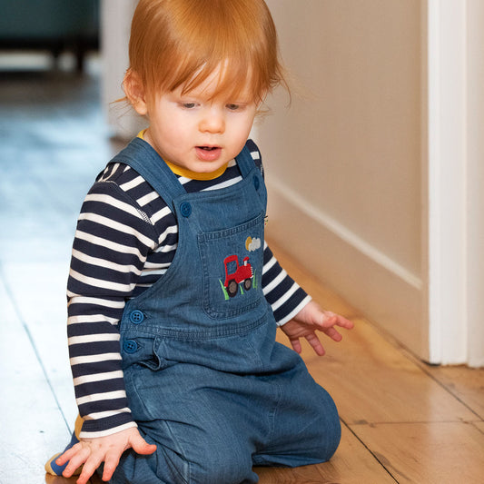 Baby wearing Frugi organic Hopscotch overalls- chambray/tractor