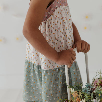 Child wearing a floral dress holding a basket of flowers against a neutral background