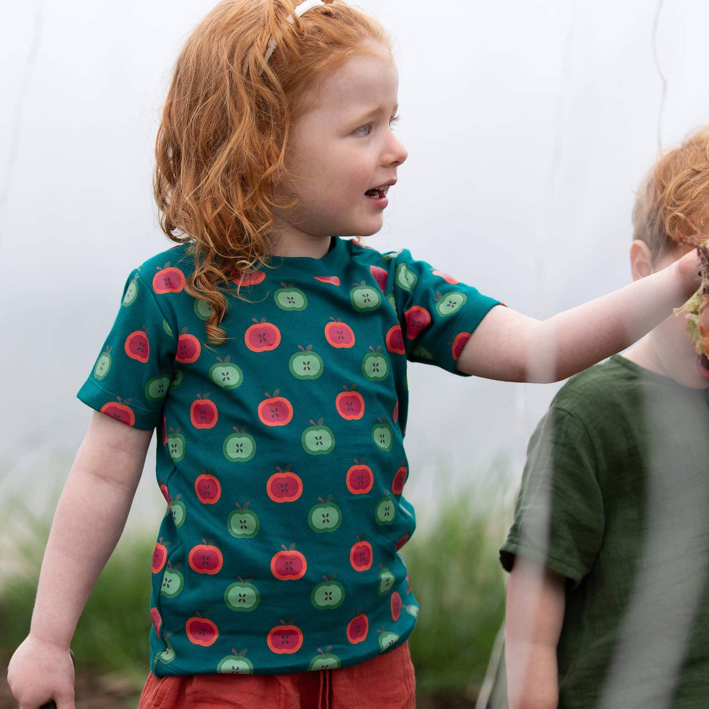 Child wearing a green t-shirt with red and green apple pattern outdoors