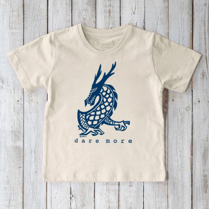 Beige t-shirt with blue dragon design and 'dare more' text on a wooden surface