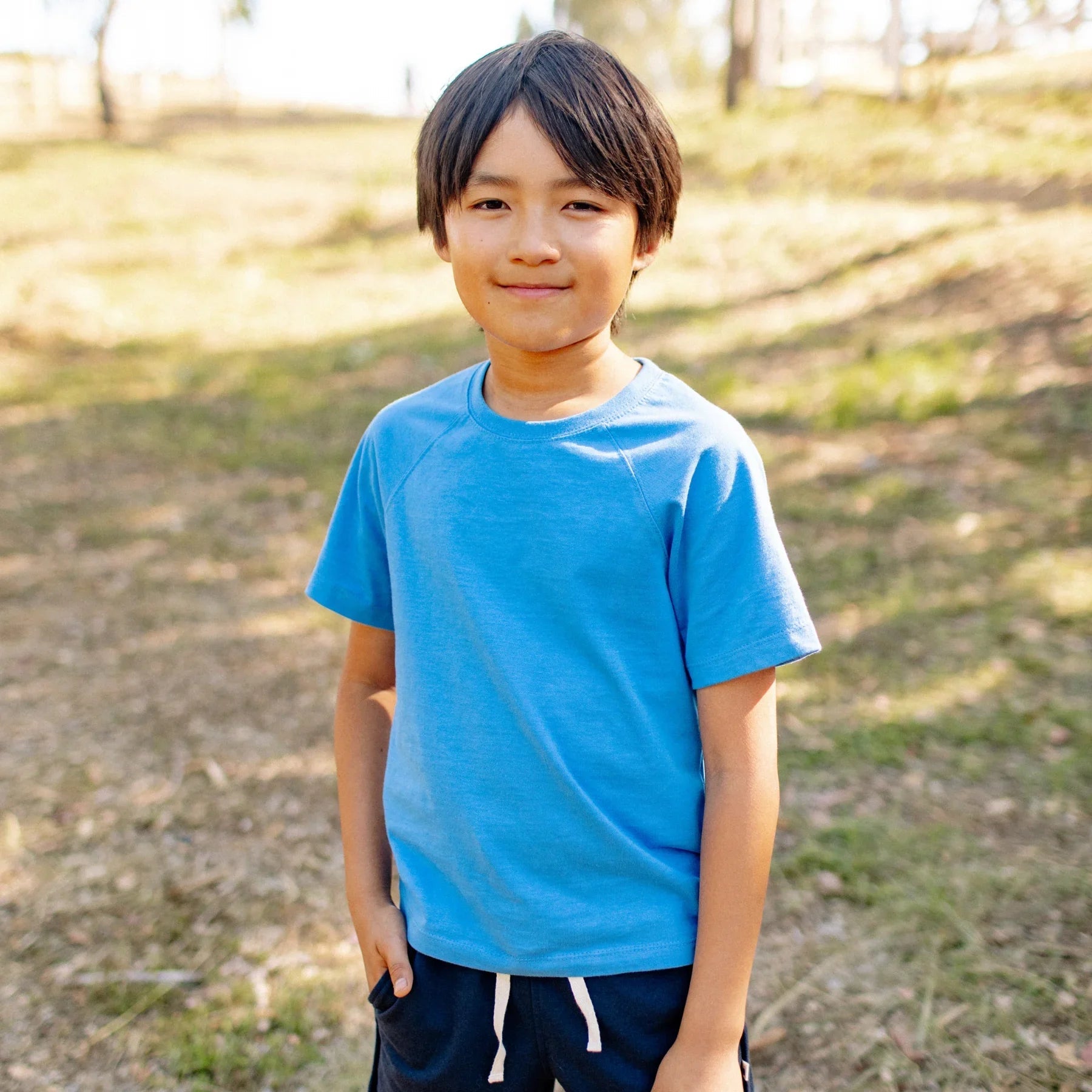 Child wearing a blue shirt standing outdoors on a grassy area