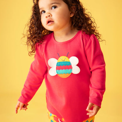 Child wearing a pink shirt with a bee design on a yellow background