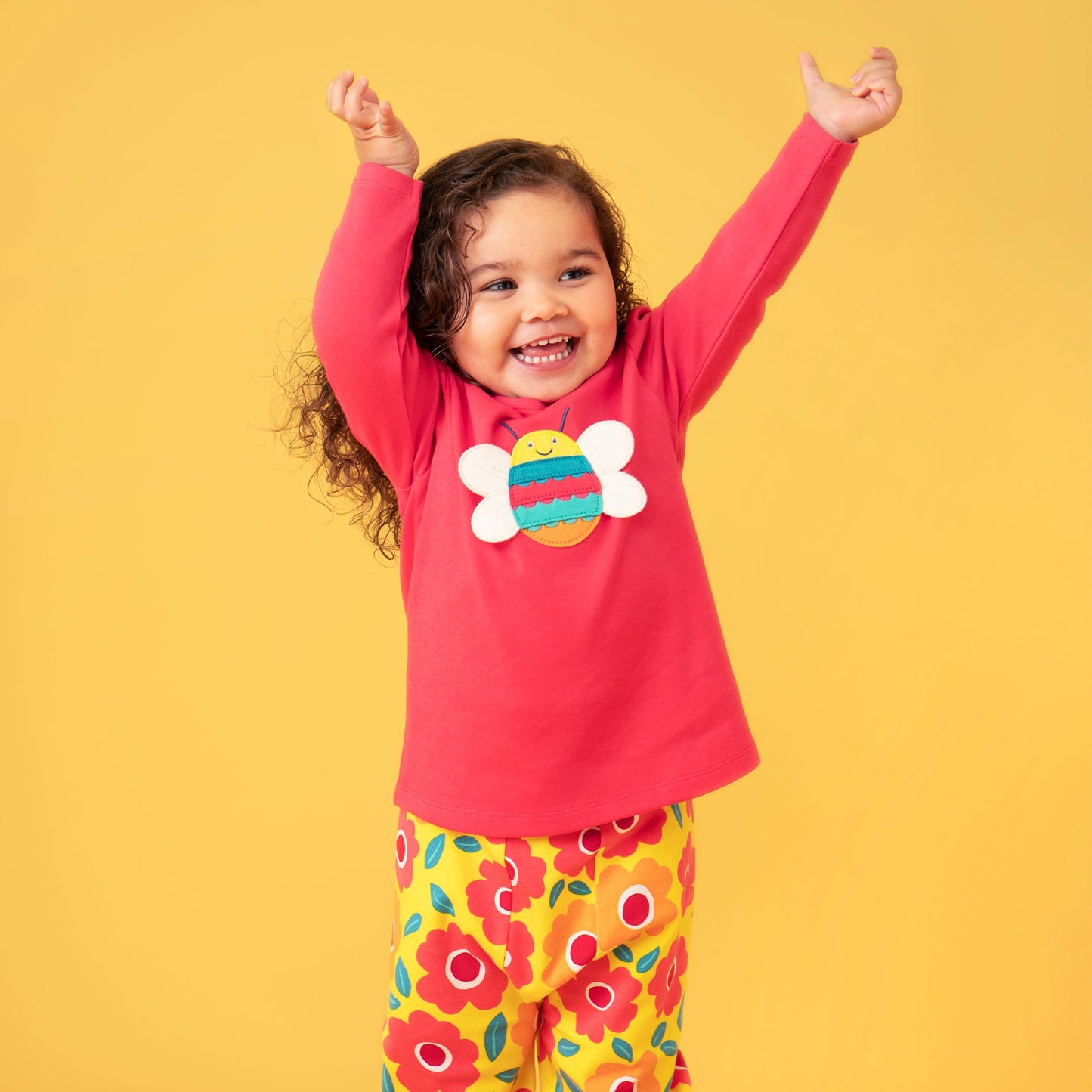 Child wearing a pink top with a colorful design and floral pants on a yellow background