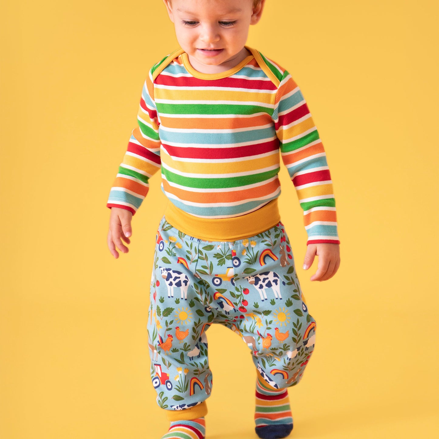 Child wearing a colorful striped shirt and farm patterned pants on a yellow background