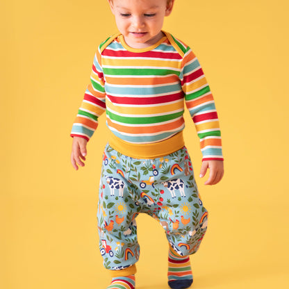Child wearing a colorful striped shirt and farm patterned pants on a yellow background