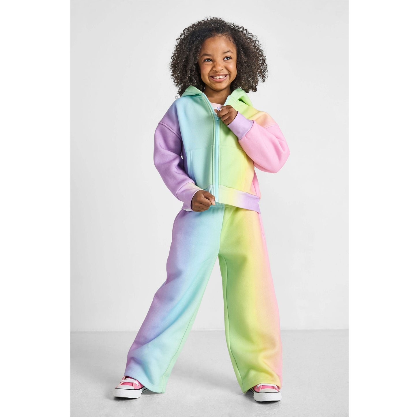 Child wearing a colorful rainbow sweatsuit set on a light gray background