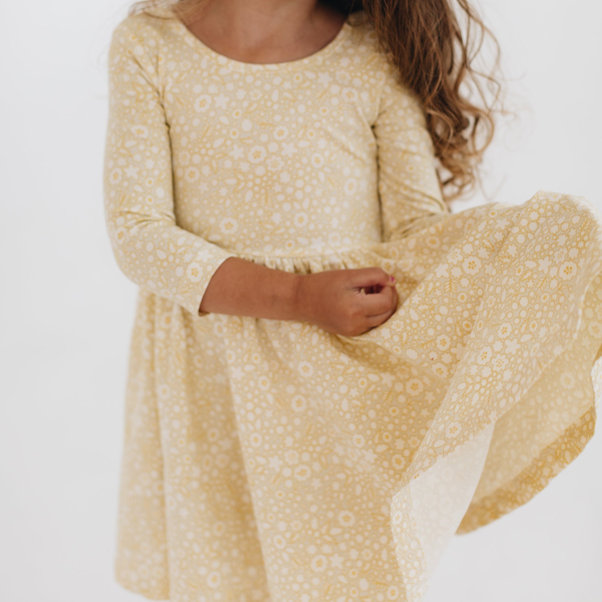 Young girl wearing a yellow floral dress against a white background