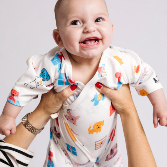 Baby in a colorful onesie being held by an adult against a plain background