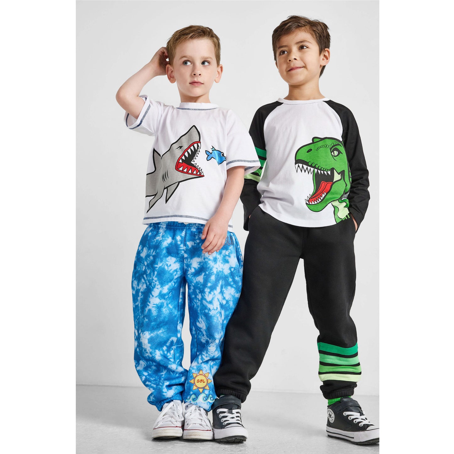 Two children wearing matching outfits with shark and dinosaur designs on a white background