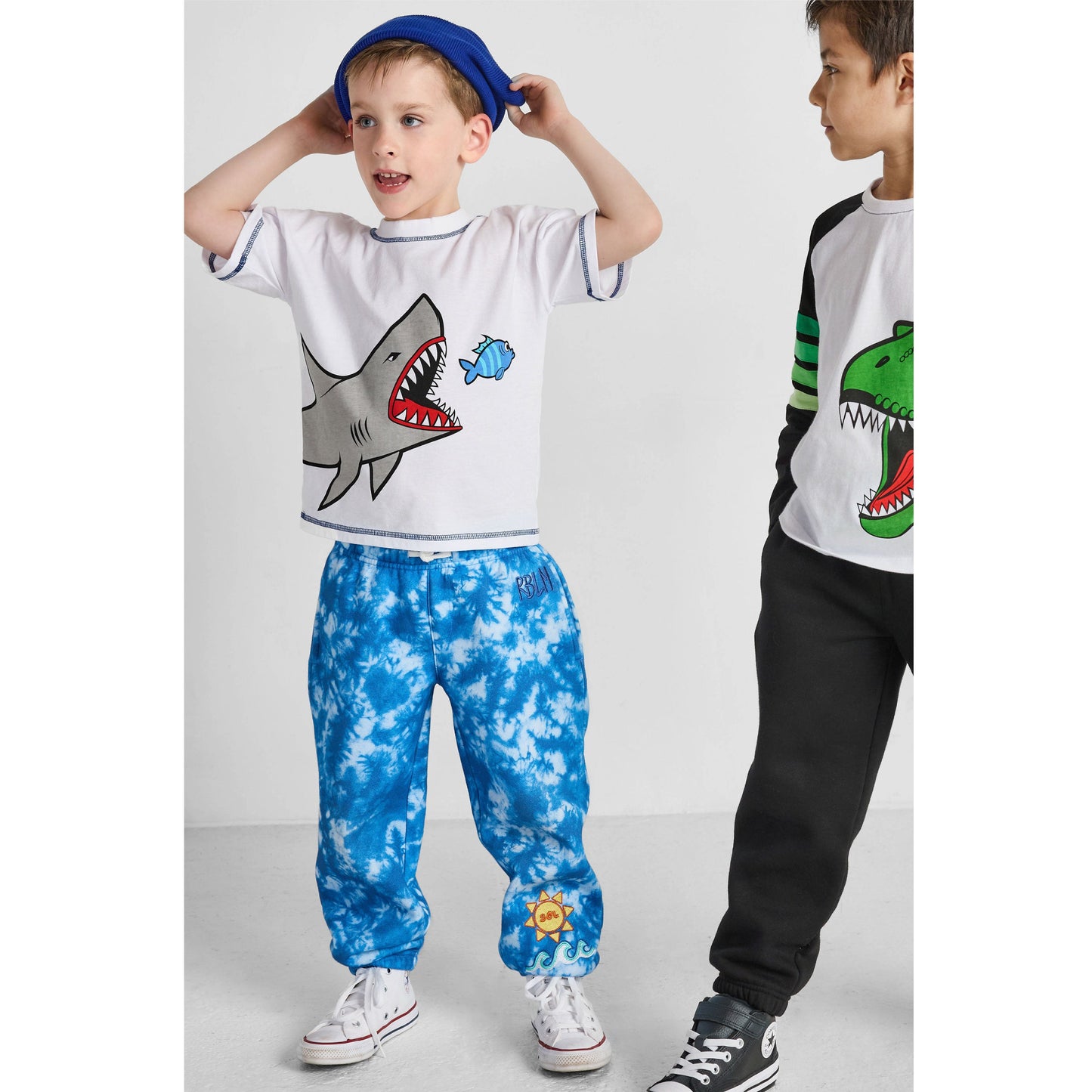 Two children wearing graphic t-shirts and colorful pants on a white background
