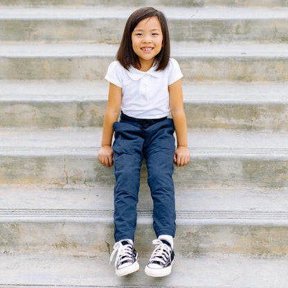 Child sitting on stone steps wearing a white shirt and blue pants.