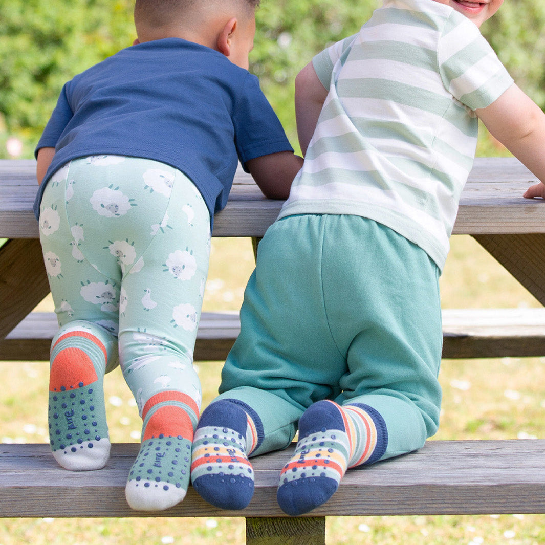 Two children sitting on a wooden bench outdoors, wearing colorful socks and pants.