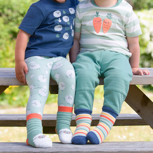 Two children sitting on a wooden bench outdoors, wearing colorful clothing and socks.