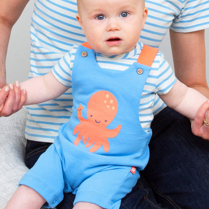 Baby wearing a blue outfit with an orange octopus design, sitting on a person's lap.