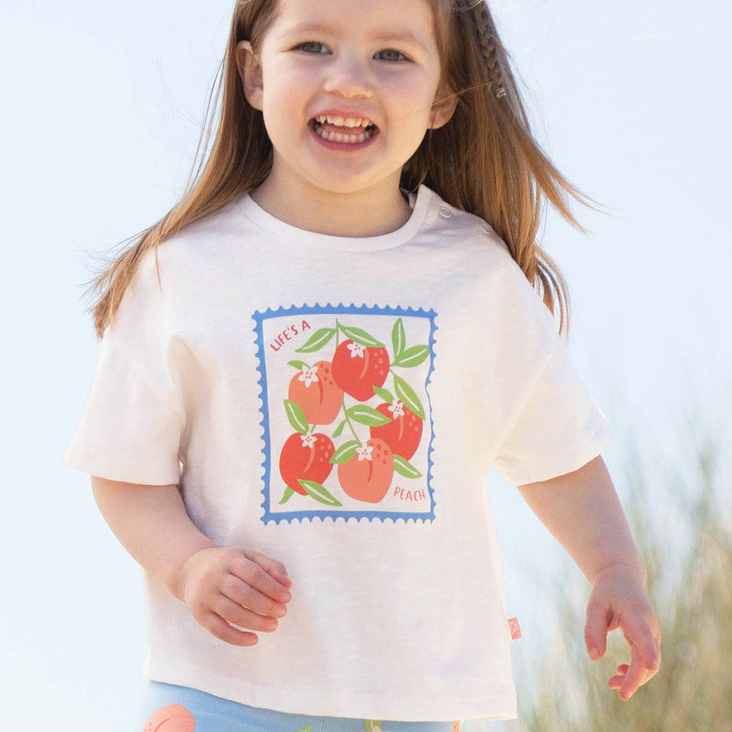 Child wearing a white t-shirt with a peach design outdoors