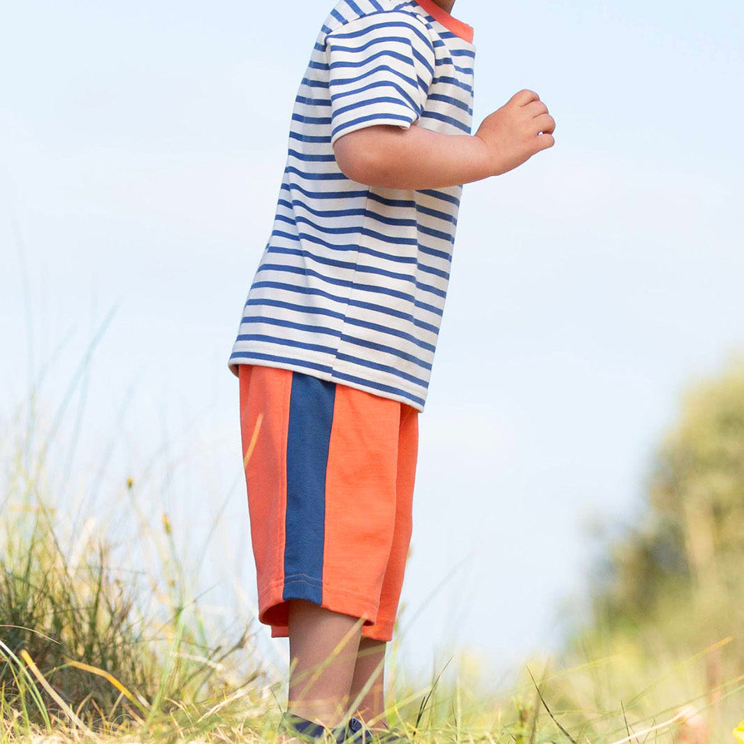 Young boy in a striped shirt and shorts standing outdoors with a clear sky.