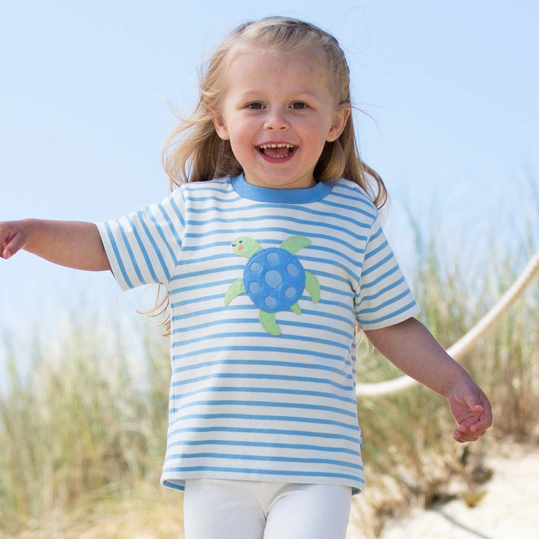 Child wearing a blue and white striped shirt with a turtle design on a beach.