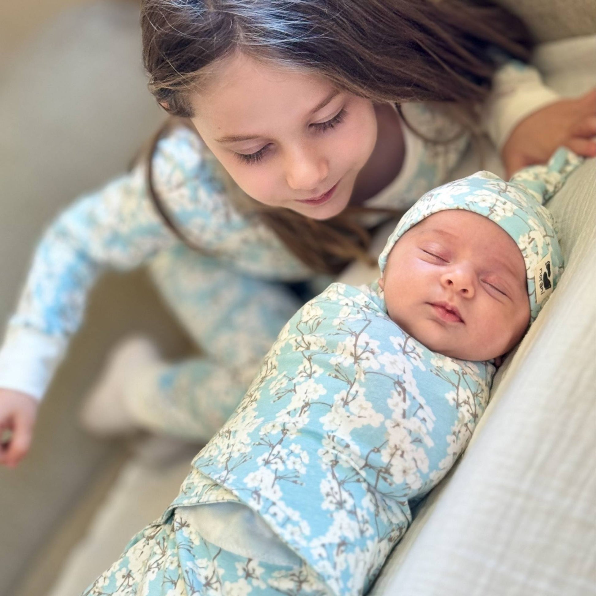 A baby swaddled in a blanket with cherry blossom design, lying next to a child.