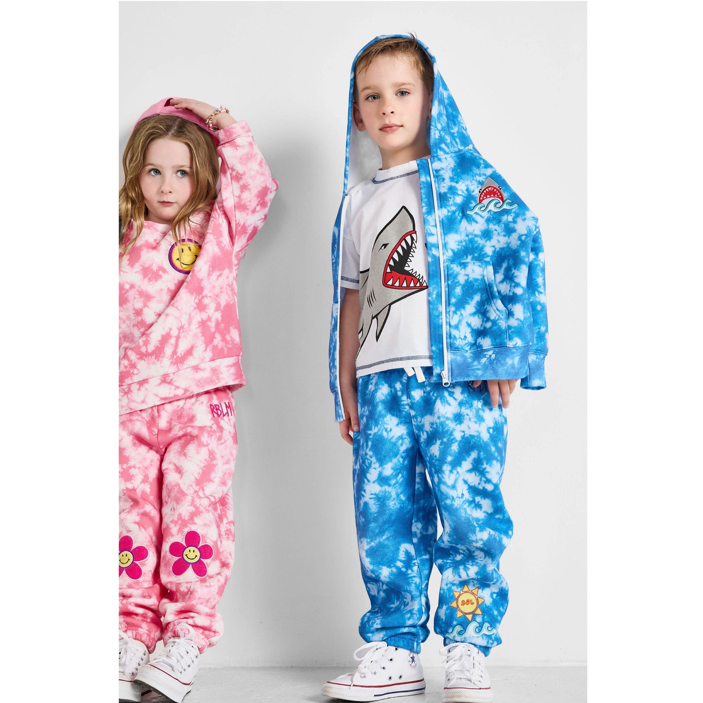 Two children wearing colorful tie-dye outfits on a plain background