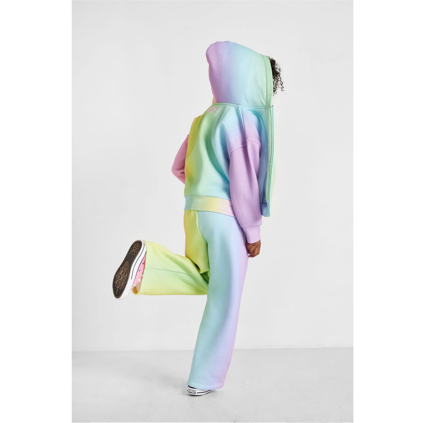 Person wearing a pastel rainbow hoodie and pants on a light gray background