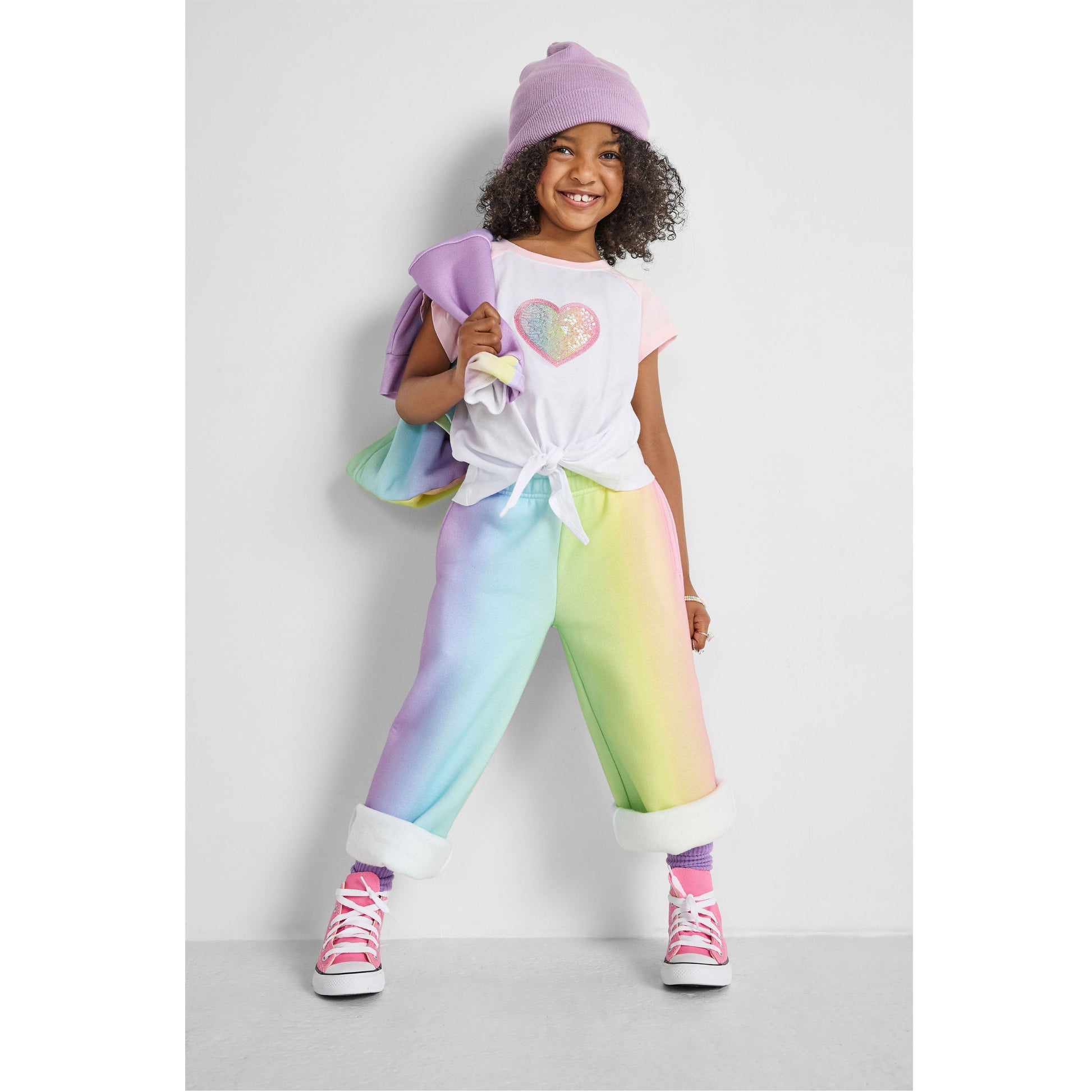 Child wearing a colorful outfit with a heart design on a plain background