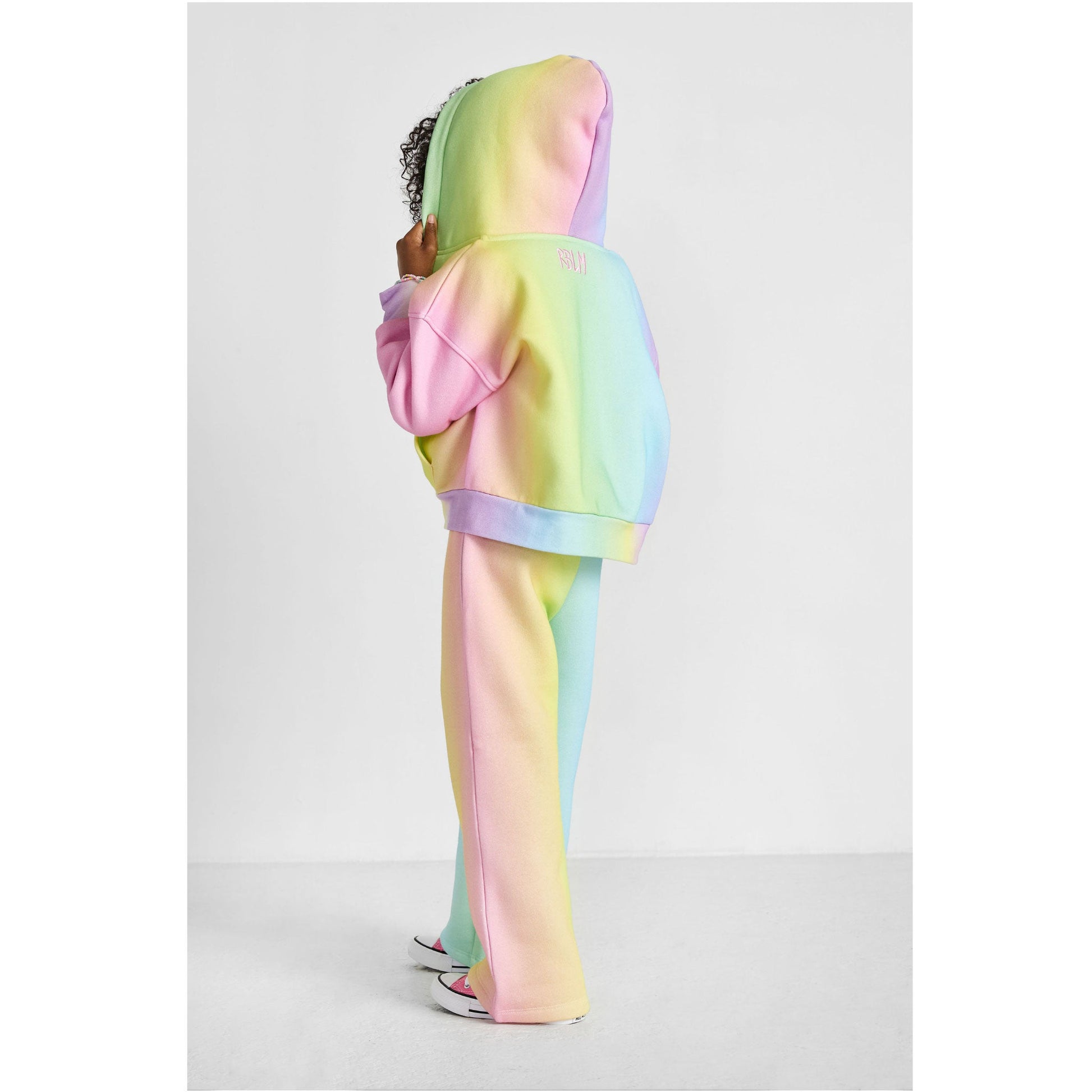 Person wearing a pastel rainbow hoodie and pants on a light gray background