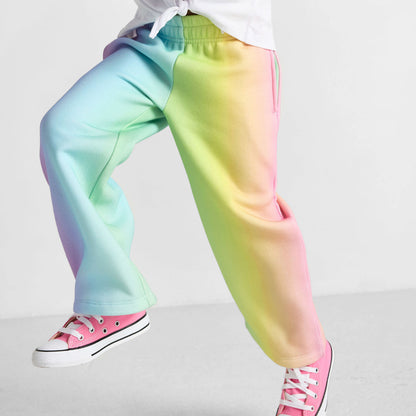 Child wearing a white top and colorful tie-dye pants on a light gray background