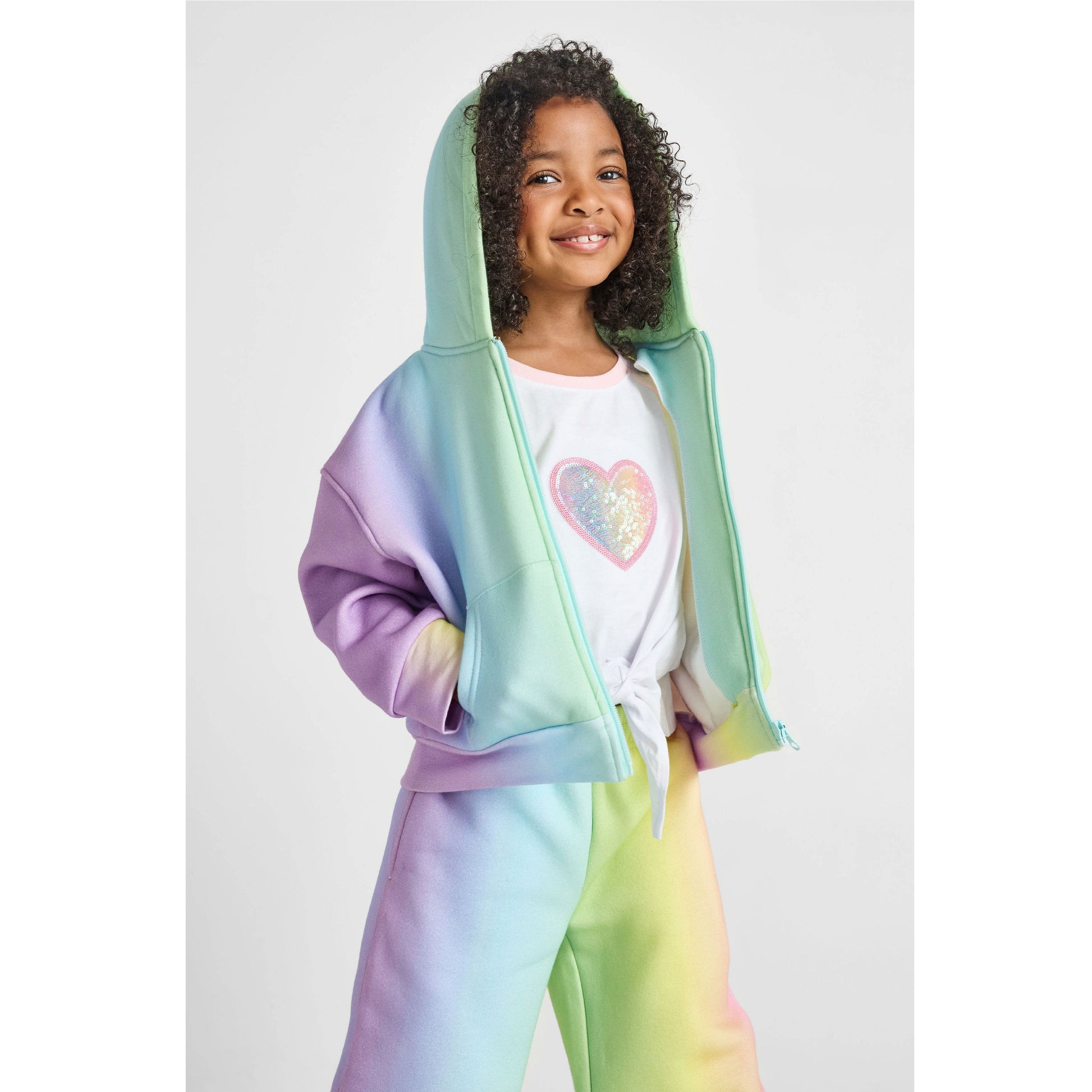 Child wearing a rainbow-colored hoodie and pants with a white shirt featuring a colorful heart design.