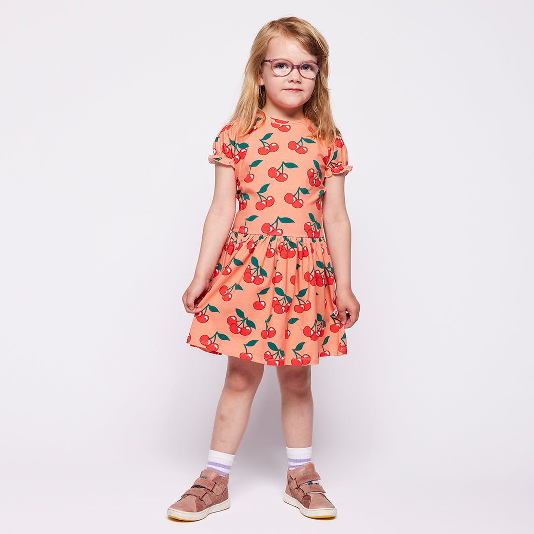 Young girl wearing a cherry-patterned dress on a plain background