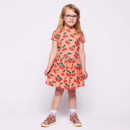 Young girl wearing a cherry-patterned dress on a plain background