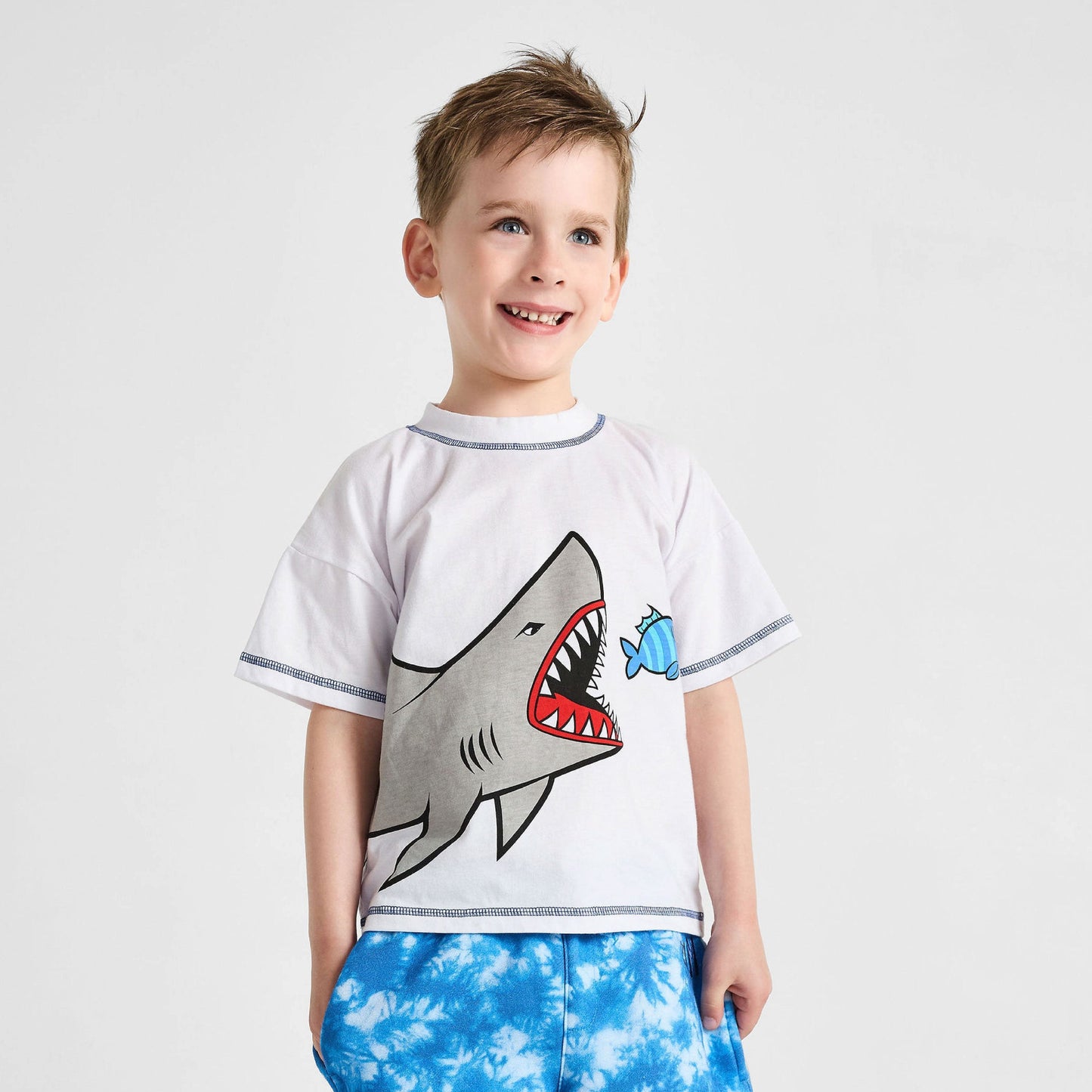 Child wearing a white t-shirt with a shark design and blue tie-dye pants on a light gray background