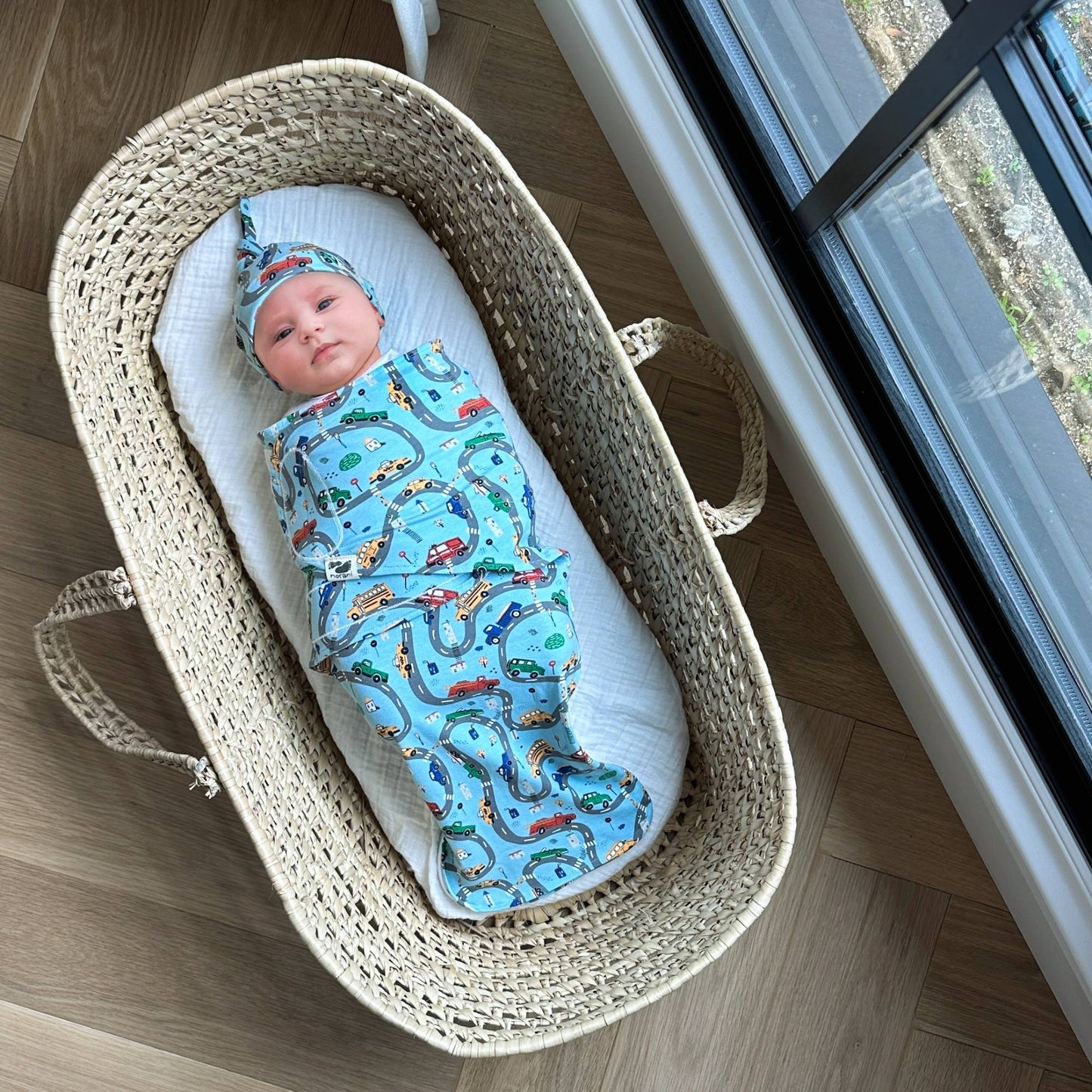 A baby swaddled in a blue blanket with car patterns, lying in a basket.