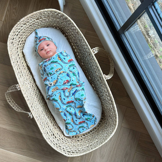 A baby swaddled in a blue blanket with car patterns, lying in a basket.