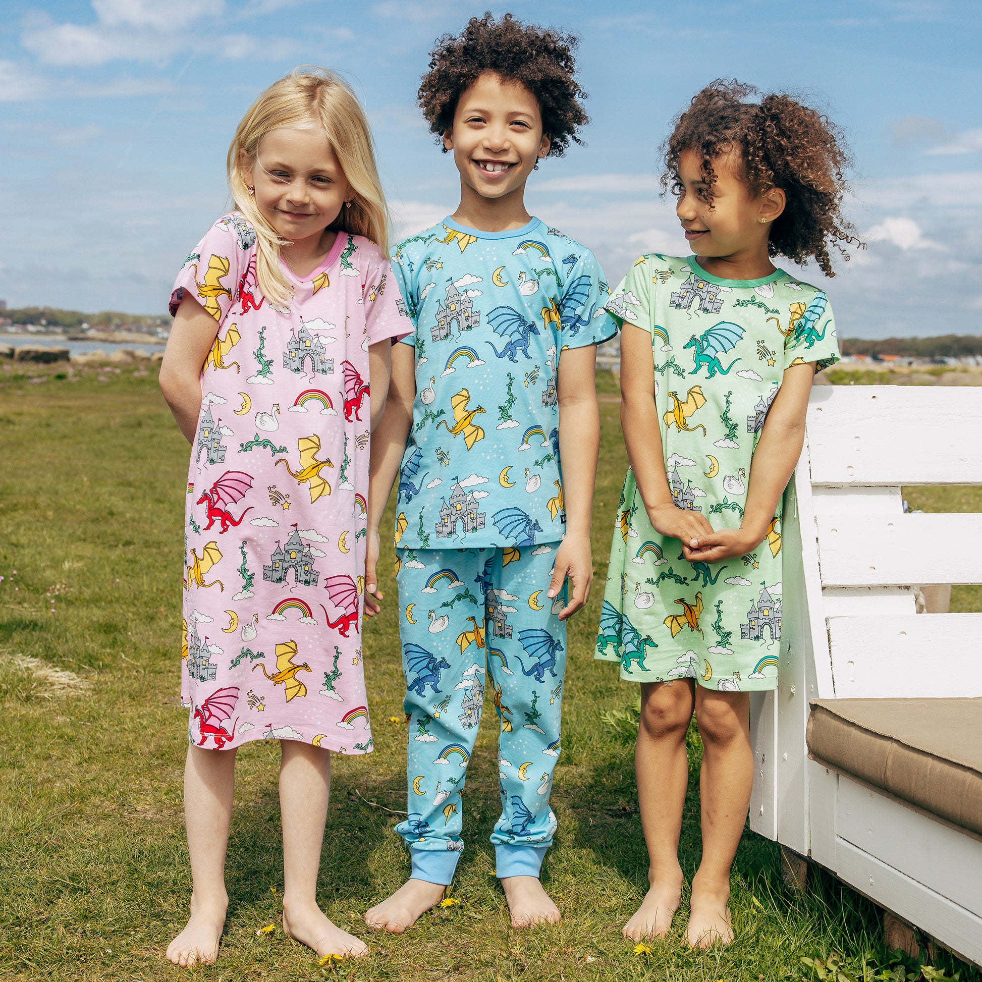 Three children wearing colorful Villervalla pajamas standing outdoors with a bench and grassy area in the background.