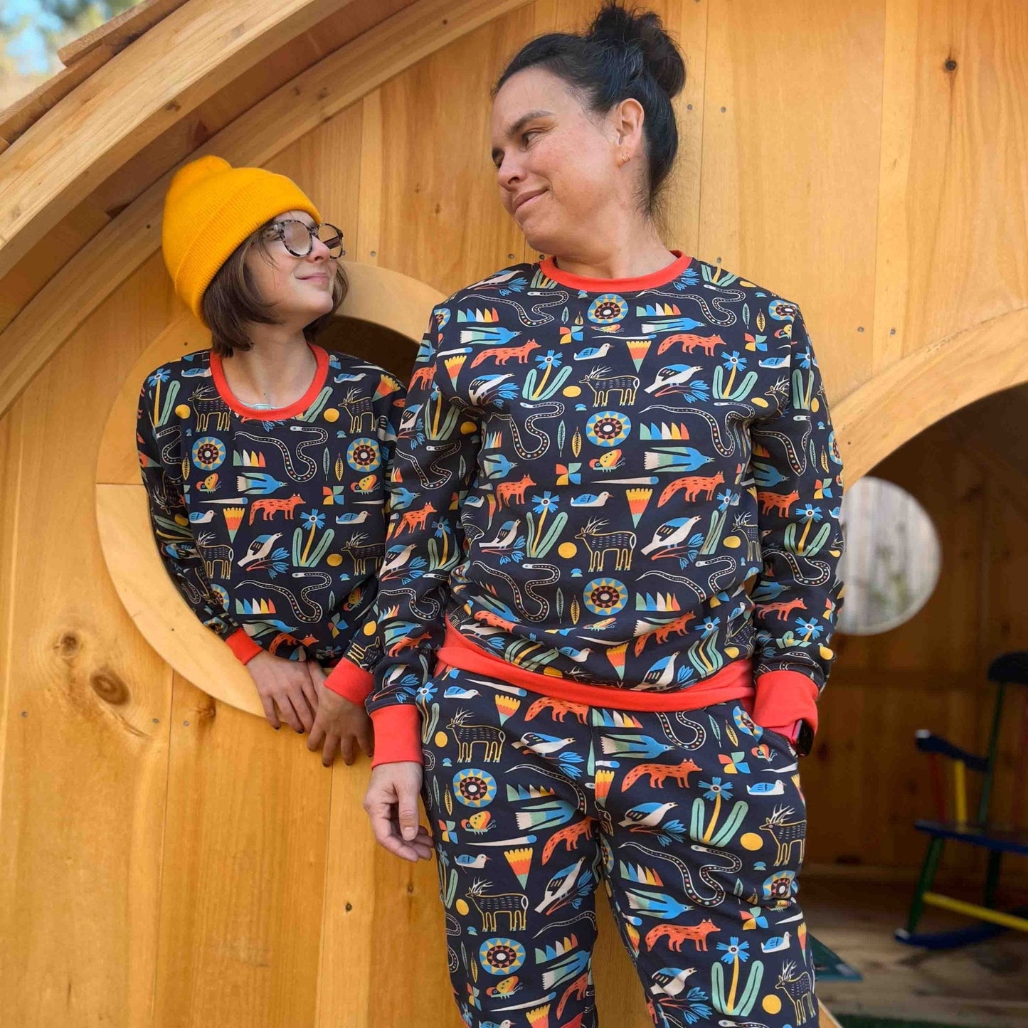 Two people wearing matching pajama sets with animal patterns in front of a wooden playhouse.