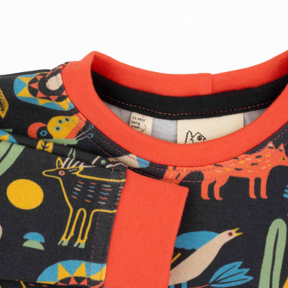 Close-up of a child's outfit with a colorful animal pattern and orange trim.